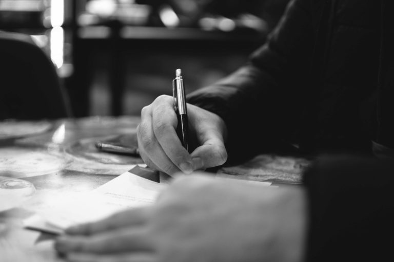 man writing on a piece of paper with pen